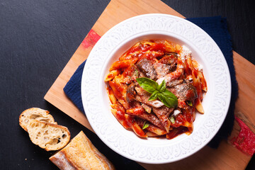 Food concept homemade organic Sicilian pasta alla norma Penne with eggplant tomato sauces on wooden board on black background with copy space