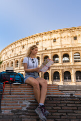 Young woman tourist searches sitting in her map for city attractions on a sunny sunny day, digital nomad, vertical shot