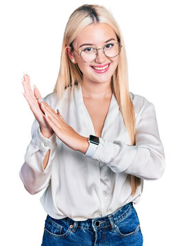 Beautiful blonde woman wearing elegant shirt and glasses clapping and applauding happy and joyful, smiling proud hands together