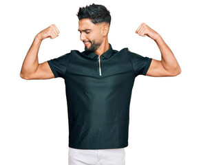 Young man with beard wearing sportswear showing arms muscles smiling proud. fitness concept.