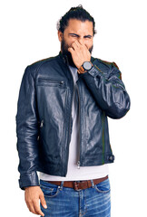 Young arab man wearing casual leather jacket smelling something stinky and disgusting, intolerable...
