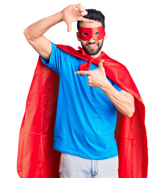 Young handsome man with beard wearing super hero costume smiling making frame with hands and fingers with happy face. creativity and photography concept.