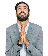Young hispanic man wearing business clothes begging and praying with hands together with hope...