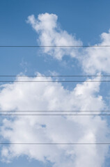 Fototapeta premium Cables of an electrical power line compose a score on a natural summy blue sky background with beautiful puffy white cumulus clouds