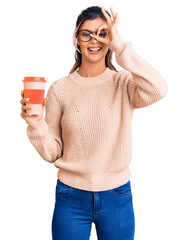 Young beautiful woman wearing glasses holding takeaway cup of coffee smiling happy doing ok sign with hand on eye looking through fingers