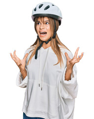 Teenager caucasian girl wearing bike helmet crazy and mad shouting and yelling with aggressive expression and arms raised. frustration concept.