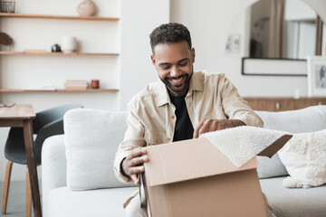 Young smiling man opening parcel at home, happy guy open package indoor, delivery and shipment...
