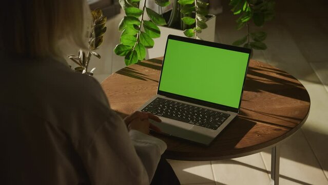 Handheld shot of an unrecognisable caucasian woman watching a laptop computer with green screen
