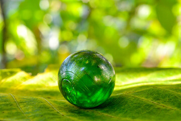 green crystal glass sphere on a sunny bokeh leaves background