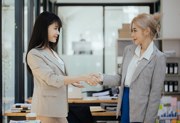 Fototapeta premium Businesswoman partnership handshake concept. Two young asian business professionals celebrating teamwork in an office, Colleague in meeting.