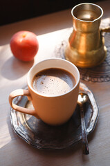 A cup of coffee with cezve and a peach on white wooden table, summer morning concept.