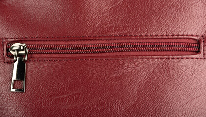 Closed zip fastening on burgundy leather surface.