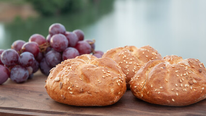 Three buns and a black grape are on the cutting board above the river.