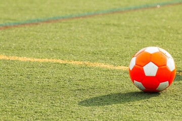 Orange soccer ball on a synthetic soccer field.
