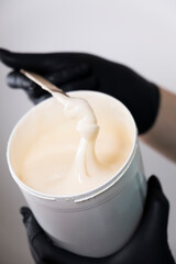 A black gloved hand wraps sugar paste for depilation with a wooden spatula