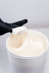 female hand in a black glove takes sugar paste for depilation from a jar