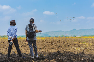 Back view of Asian mothers look with worry and concern during parachute training from airplane for army cadet with blurred image of parachute and landscape in background. Family relationship concept.