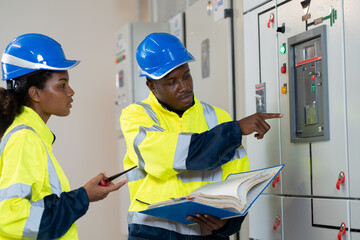 Team of electrician engineer maintenance electric system with manual book in control room. Group of African American electrician engineer checking electric system in control room