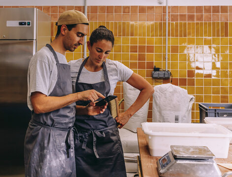 Bakers using smartphone during work in workshop