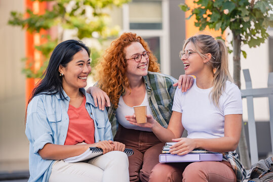 A diverse group of cheerful female college students sitting in front of a university building, talking, smiling