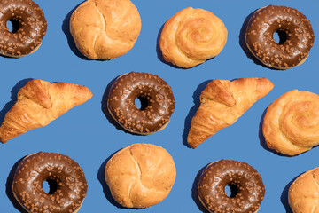 Pattern of pastries, donuts,croissant and a pie on blue background. Flat lay, top view