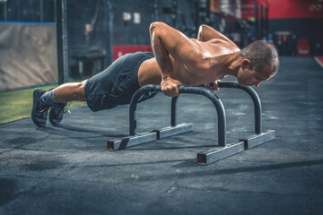 Fit and muscular man doing horizontal push-ups with parallel bars in gym.