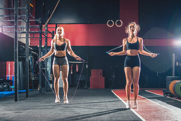 Two attractive girls exercising with jumping rope together in the gym
