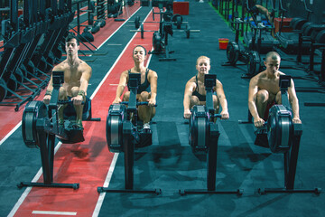 Naklejka premium Group of sporty people working out on the rowing machines at the gym.