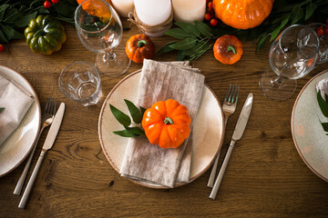 Autumn table setting with craft plate, cutlery, pumpkin and candles at oak table. Thanksgiving food festive dinner concept. Top view with copy space.