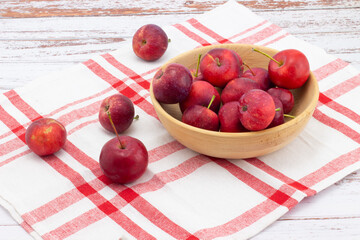 Still life with fresh small apples in wooden bowl on a red and white checkered linen napkin. Wild red crabapples in bowl on wooden tabl