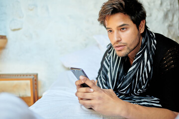 Stylish Hispanic man chatting on smartphone on bed
