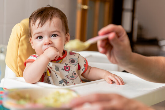 Anonymous mother feeding baby with porridge in kitchen