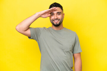 Young Arab handsome man isolated on yellow background saluting with hand with happy expression