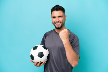 Young Arab handsome man isolated on blue background with soccer ball celebrating a victory
