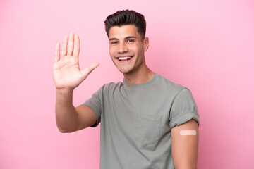 Young caucasian man wearing band-aids isolated on pink background saluting with hand with happy expression