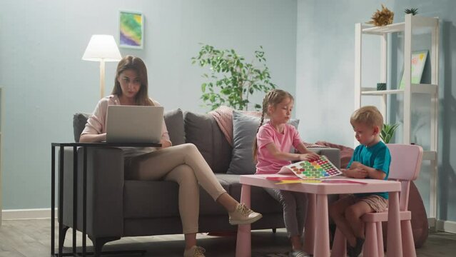 woman works at laptop at home, children next to their mother