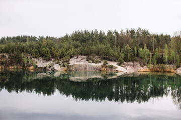 Obraz premium Clean mountain lake, on the other side of the cliff and a pine forest. Forest and mountains are reflected in the water. Overcast weather.