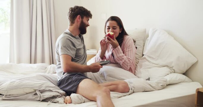 Couple eating a cupcake for birthday breakfast in bed to celebrate with cake in bedroom of vacation home and giving gift for love in morning. Happy man and woman celebrating anniversary with food