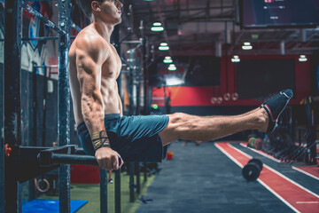 Cropped photo of young handsome shirtless man's body in L Sit position on parallel bars during Calisthenic workout at gym.