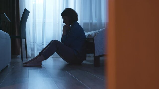 Lonely and sad woman sits in a dark room. The concept of a person in a state of depression or stress. Violence in family.