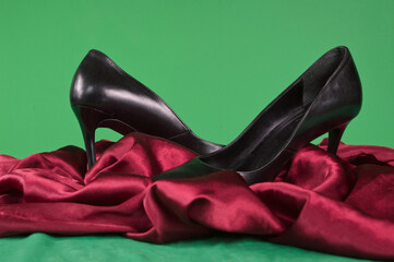 Fototapeta Czarne szpilki buty na czerwonej satynie i zielonym tle obraz