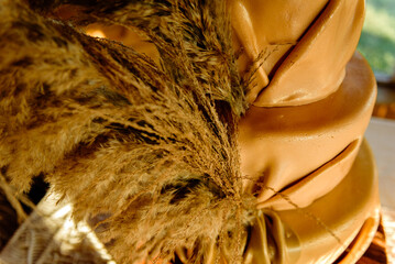 A tan cake draped in icing that resembles leather and decorated with pampas grass