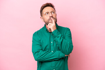 Middle age caucasian man isolated on pink background having doubts while looking up