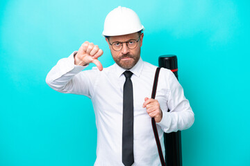 Middle age architect man with helmet and holding blueprints isolated on blue background showing thumb down with negative expression