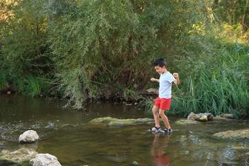 child crosses a river with a low riverbed in summer. Adventure games