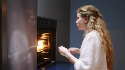 Young woman takes chocolate pie out of the oven. Girl makes pastry at home. Female performs homemade baking in stylish modern kitchen. Housewife prepares and smells dessert, smiles on camera closeup