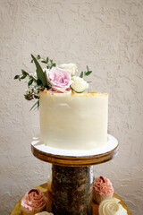 Rustic white one tier wedding cake with pink and white roses and greenery sitting on a wooden stand