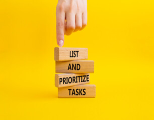 List and prioritize tasks symbol. Concept words List and prioritize tasks on wooden blocks. Beautiful yellow background. Businessman hand. Business and List and prioritize tasks concept. Copy space.