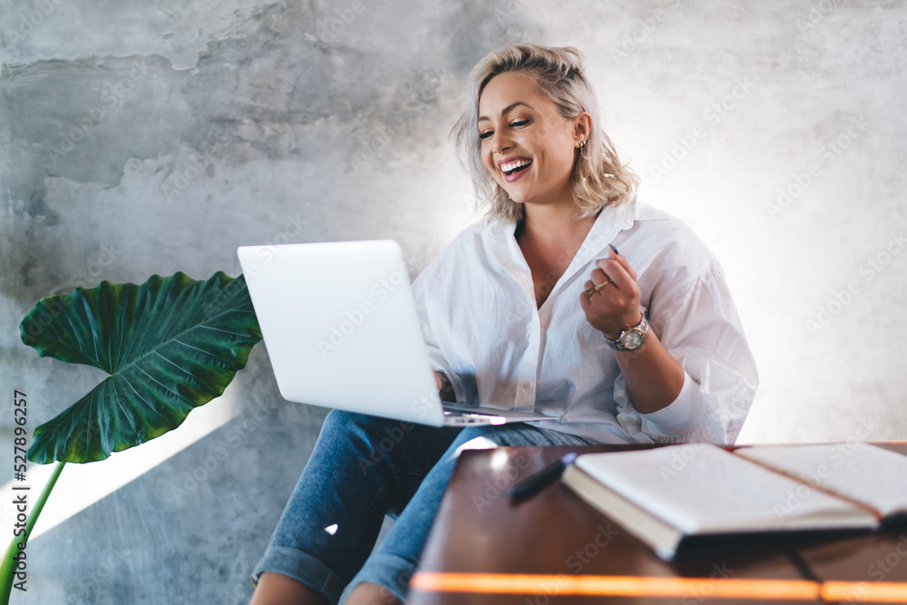 Poster millennial female blogger browsing media in social networks using laptop device and smiling, cheerfu