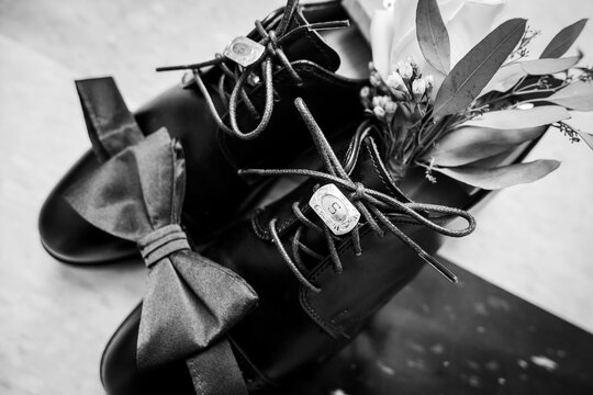 Black and white image of groom's shoes with bowtie and cuff links resting on top
